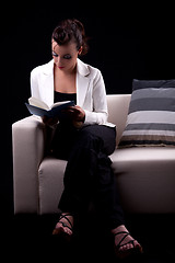 Image showing Beautiful woman seated on couch reading a book