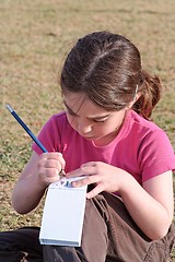 Image showing Cute little girl with pigtails writes outdoor 