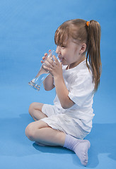 Image showing Small cute girl is drinking water on blue background