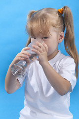 Image showing Small cute girl is drinking water on blue background