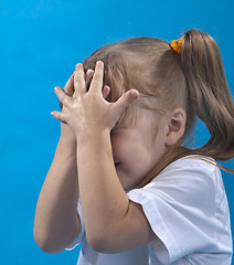 Image showing Small girl is covering her face by hands isolated on blue