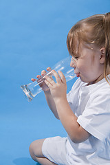 Image showing Small cute girl is drinking water on blue background