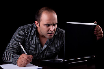 Image showing surprised businessman looking to computer and taking notes