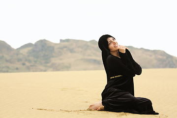 Image showing Woman in shawl sitting on sand looking up