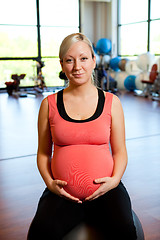 Image showing Pregnant woman sitting on fitness ball holding belly.