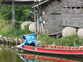 Image showing Longtail boat on a canal in front of straw house in Thailand