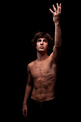 Image showing young man in topless looking up to the light and raising arm - sign of faith 