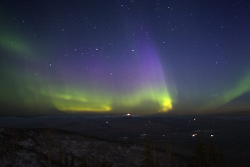 Image showing Purple-green-yellowish northern lights in starry sky over hill t