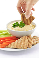 Image showing Hand dipping pita in hummus