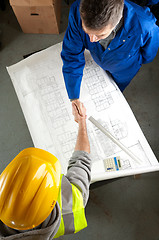 Image showing Two builders shake hands over blueprint