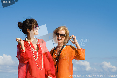 Image of two beautiful women hearing shells on beach