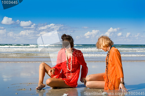 Image of two beautiful women sitting on beach