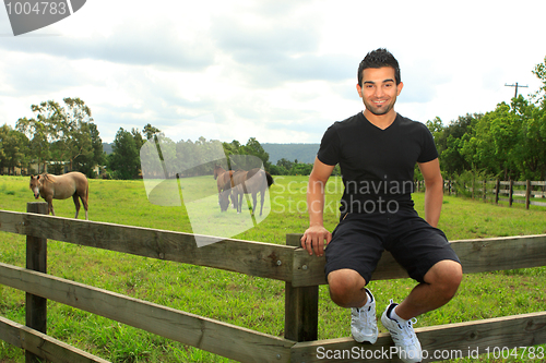 Image of man sitting on fence of a horse paddock