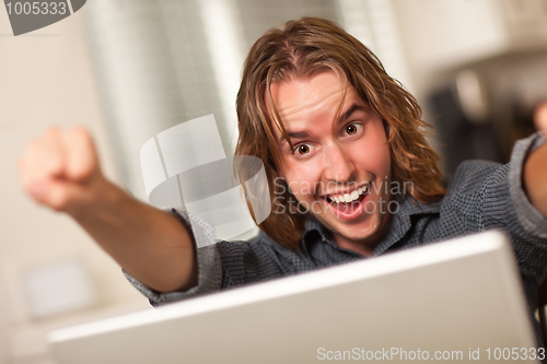 Image of Cheering Young Man Using Laptop Computer