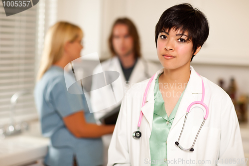 Image of Pretty Latino Doctor Smiles at Camera as Colleagues Talk