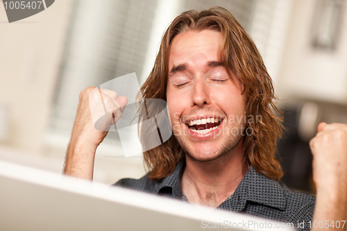 Image of Cheering Young Man Using Laptop Computer