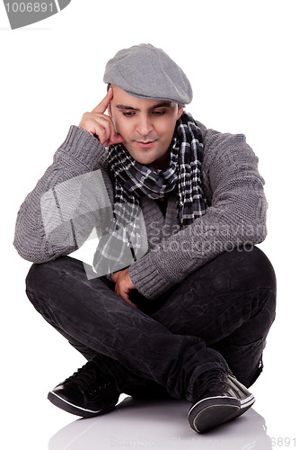 Image of Portrait of a young man sitting on the floor, thinking and looking down, in autumn/winter clothes