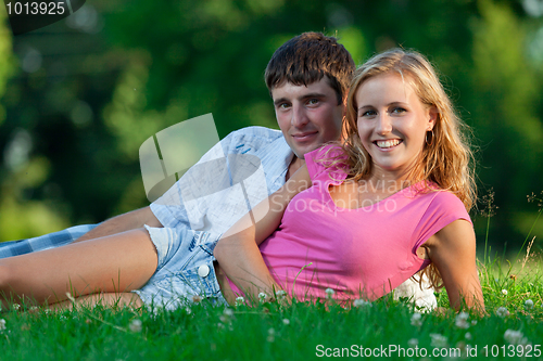 Image of A couple relaxing in the park, lying on the grass, lit in the ev