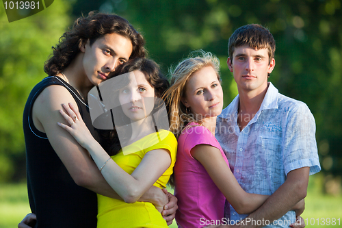 Image of Four young people embrace and stand in the park