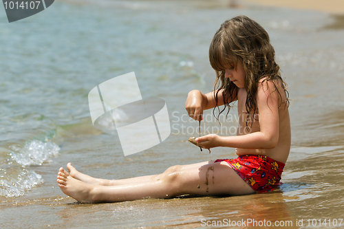 Image of The little girl is sitting on a beach in the waves