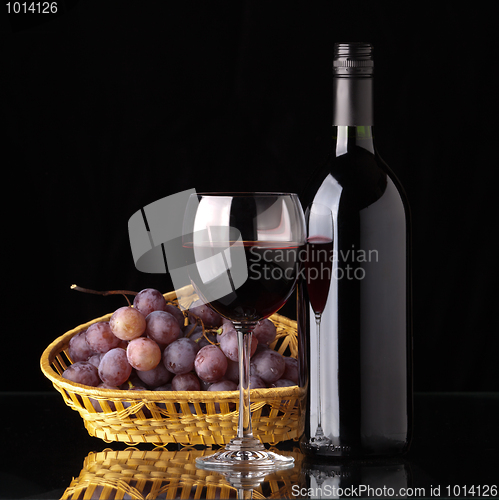Image of A bottle of red wine, glass and grapes