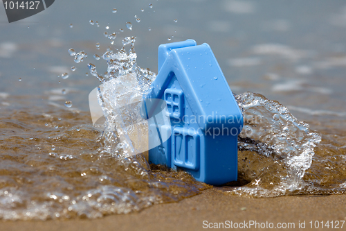 Image of Toy plastic house on the sand washes wave