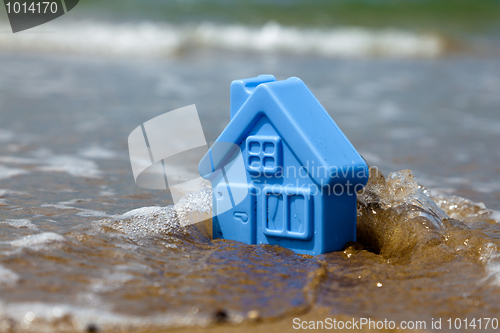 Image of Toy plastic house on the sand washes wave