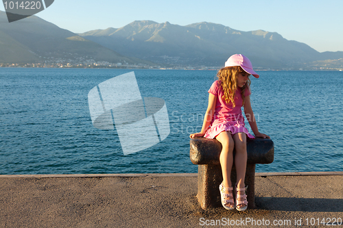 Image of The little girl in a pink dress sitting on a bollard in the mari