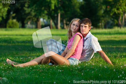 Image of Two young lovers sitting on the lawn in the park and looks into 