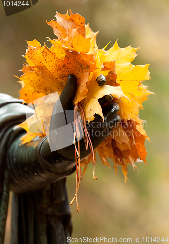 Image of A bouquet of yellow autumn leaves in the hands of a bronze statu