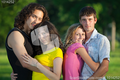 Image of Four young people embrace and stand in the park