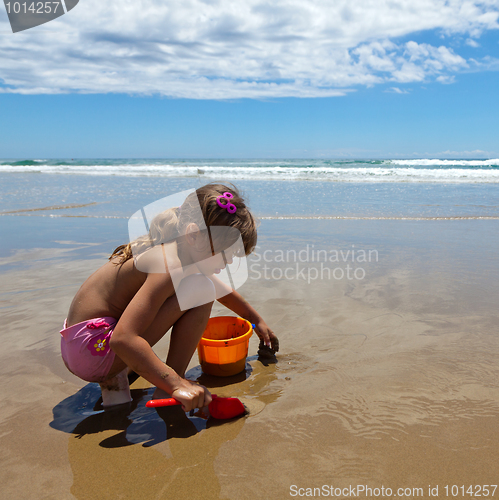 Image of A girl playing on the wet sand with a shovel and pail