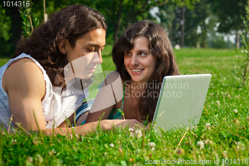 Image of The boy and girl lying on the grass in the park with a laptop