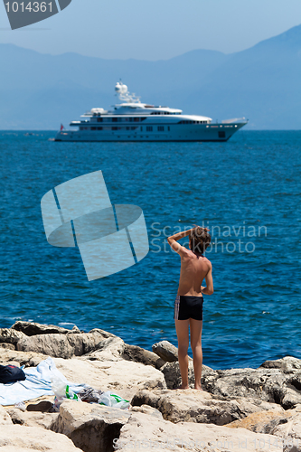 Image of A boy on a brick bank admires luxury white yacht