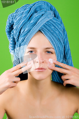 Image of woman in blue towel applying facial cream