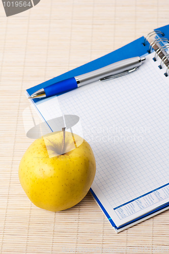 Image of Open notebook, yellow apple and pencil 
