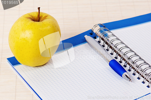 Image of Open notebook, yellow apple and pencil 