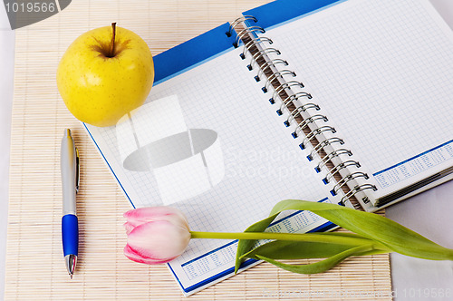 Image of Open notebook, yellow apple and pencil 