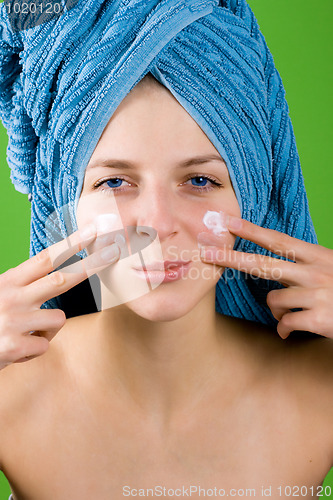 Image of woman in blue towel applying facial cream