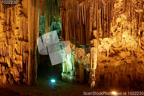 Image of Young woman touching huge stalactites in colorful Melidoni Cave