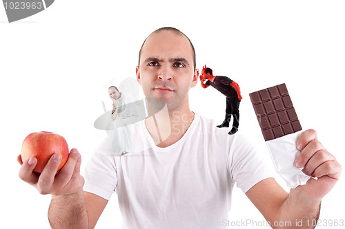 Image of young man torn between eating an apple and a chocolate,between the devil and angel,