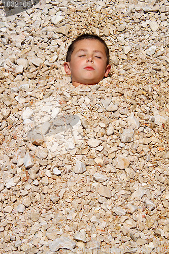 Image of boy buried in the pebbles on the beach