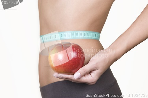 Image of woman holding an red apple while measuring her waist