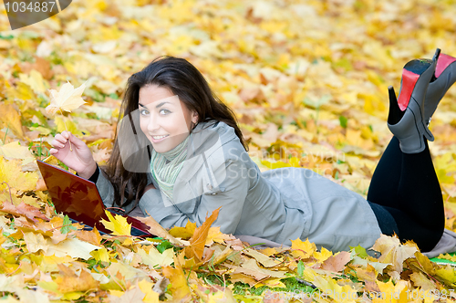 Image of Happy student girl lying in autumn leaves with netbook