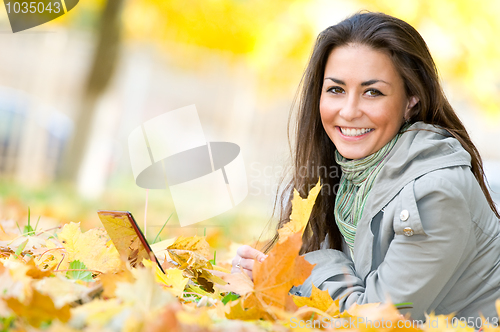 Image of Happy student girl lying in autumn leaves with netbook