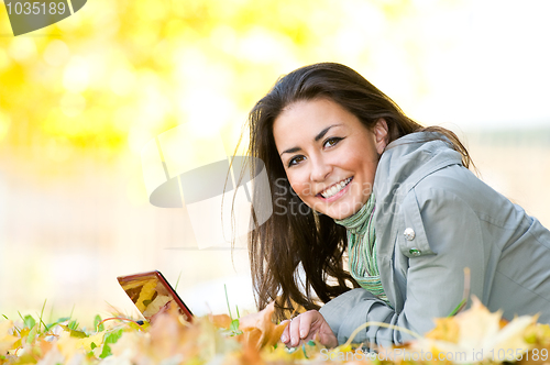 Image of Happy student girl lying in autumn leaves with netbook