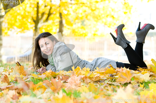 Image of Happy student girl lying in autumn leaves with netbook