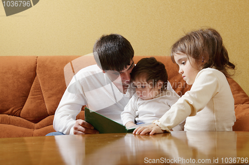 Image of Father reading book to daughters