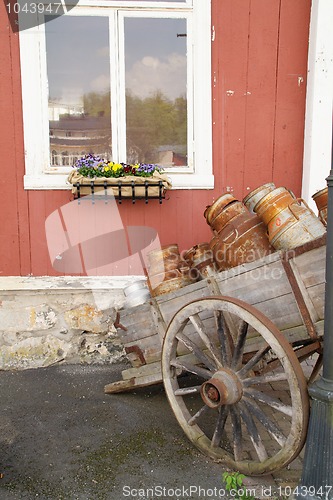 Image of Old cart with milk cans near the house