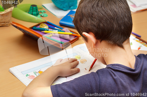 Image of boy doing homework  with color pencil, painting fruits